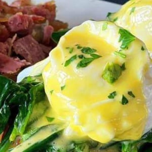 Eggs and greens with meat and potatoes on the side on a white plate